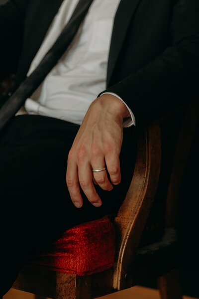 A groom lounges in a vintage velvet chair showing off his new wedding ring.