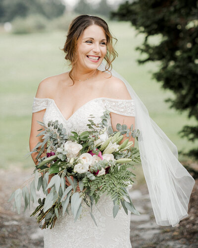 Bride holds her bouquet and laughs as her veil is caught in the wind