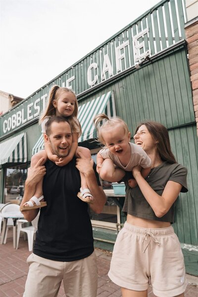 Wedding photographer plays with her husband and two little girls in small town Minnesota main street