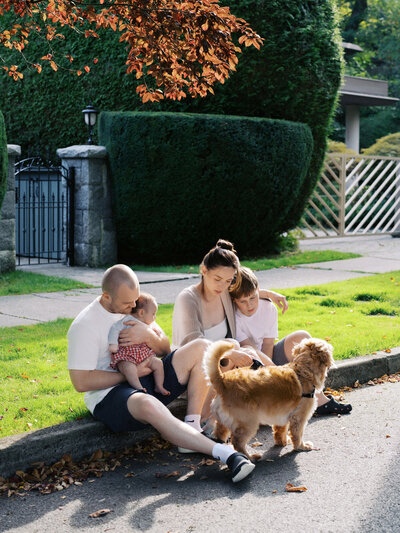 Mother and father kissing and playing with their newborn baby at a park in Squamish