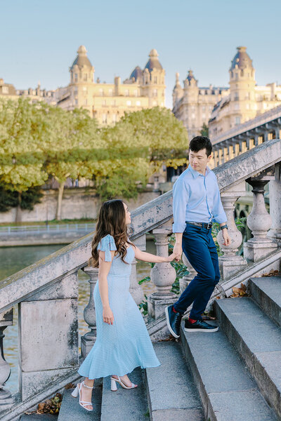 Couple holding hands walking up steps by Eiffel Tower during photoshoot in Paris