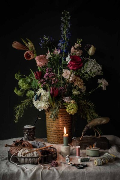 Stilleven met groot gekleurd bloemstuk met vlinder in vaas (west germany) van aardewerk met rondom brei en naai attributen zoals wol, breinaalden, meetlint en garen