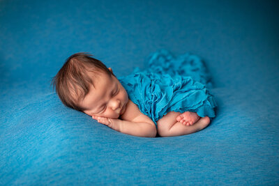 Sweet baby girl posed on a beautiful blue  backdrop during her newborn session.