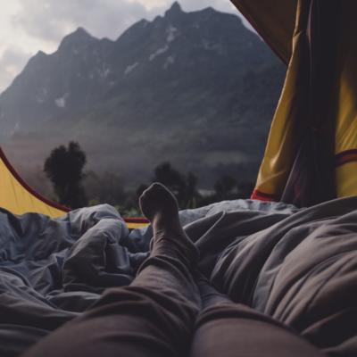 Looking down a persons legs through an open tent at a mountain view.