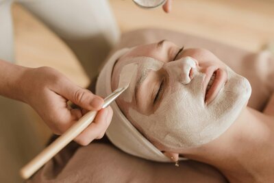 Jennifer is applying a masque to a woman's face during a facial.