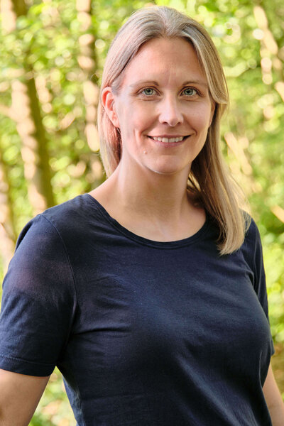 Freundliches Portrait der professionellen Wellness-Masseurin Jennifer Okroy im Wald stehend