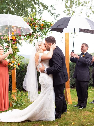 Bride and groom share their first kiss during their rainy outdoor ceremony.