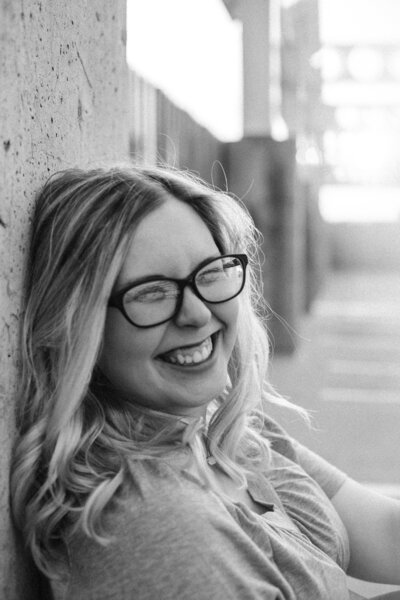 A black and white photo of a young women smiling with glasses.