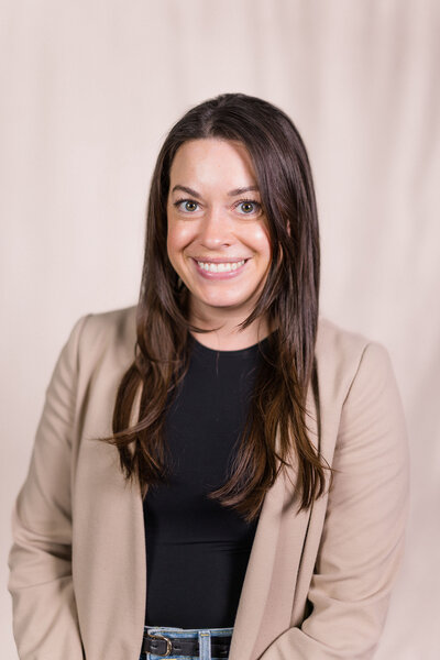 A professional headshot of Emily Austin, LCSW, smiling at the camera in a black shirt and beige blazer, representing her expertise in therapy.