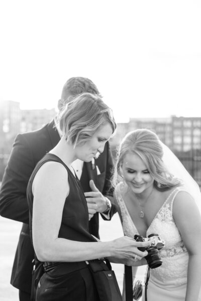 black and white image of wedding photographer showing the back of her camera to wedding couple