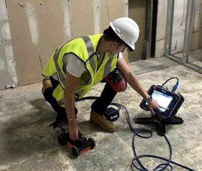 An operator in a safety vest and hard hat operates a Ground Penetrating Radar (GPR) scanner.