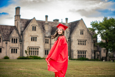 Joyful senior photos Pittsburgh shot of student wearing a red cap and gown in front of the Hartwood acres Manor.