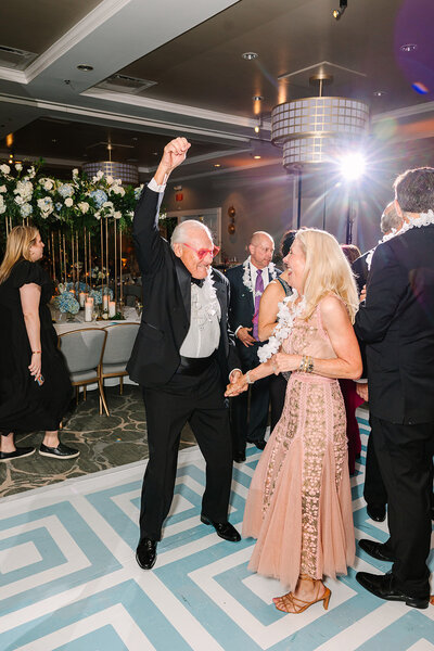 Flash photo of guests dancing on a blue and white dance floor and wearing pink heart sunglasses