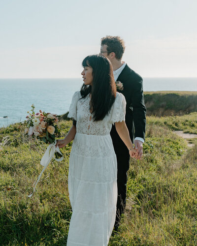 A couple holds hands in front of a coastal view during their elopement