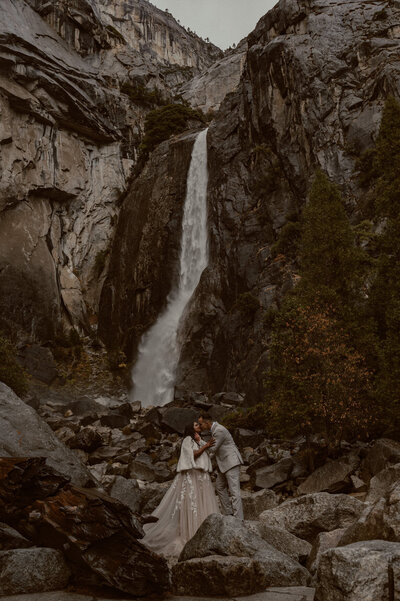 bride and groom kissing beneath lower yosemite falls