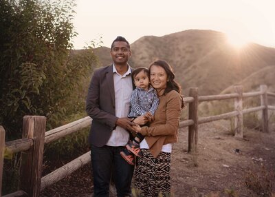 Mom, Dad, and Toddler smiling at the camera at golden hour with the Elsinore mountains in the distance.