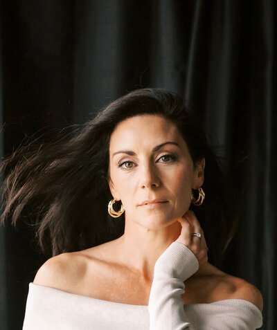 Creative headshot of brunettee makeup artist against black backdrop hair blowing in wind.
