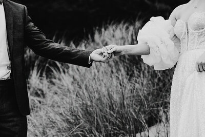 Candid black and white photo of couple holding hands in grassy field - Aim True Photography