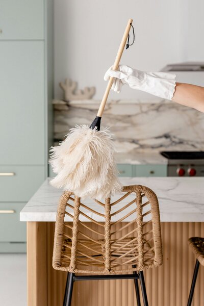 a professional house cleaner wearing white gloves and cleaning a chair with a duster 