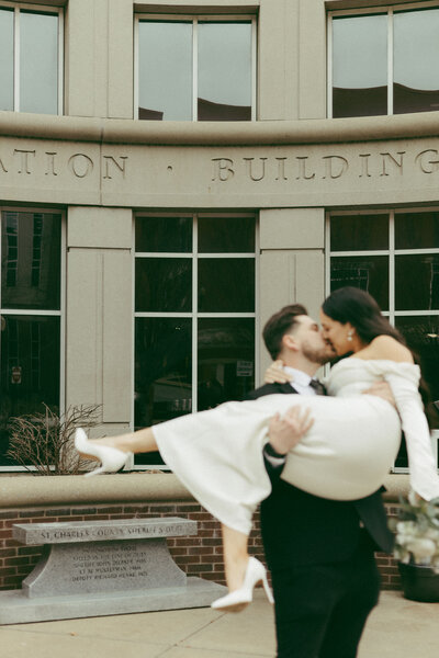 A groom picking up his bride in front of a city hall with a film aesthetic, shot by Stacey Vandas Photography.