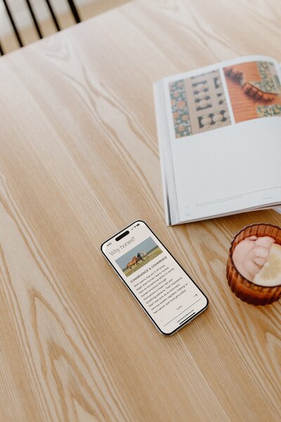 Clean, modern mobile website design for equine therapy website with a warm, minimalist aesthetic displayed on a phone over a natural wood surface.