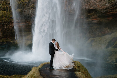 Utah Wedding Photographer captures outdoor wedding with bride and groom embracing by waterfall