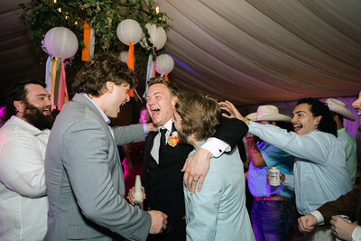 Groom in classic tuxedo hugs guests under paper lanterns on the dance floor, surrounded by joyful energy and editorial lighting at a luxury Austin celebration.