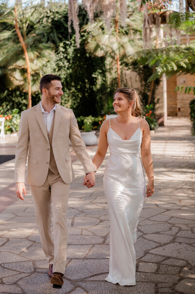 Couple walks hand in hand towards the camera smiling at one another.