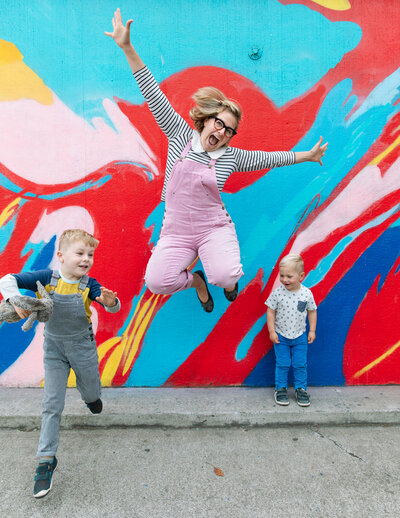 mom with two young boys jumping in front of a colorful mural in oakland