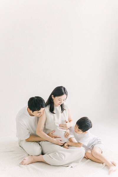 妊婦さんのママのおなかに、パパとお兄ちゃんが手を添えて三人でおなかを見つめている、おしゃれなマタニティフォト。新宿区のスタジオでYukika Ishikawa Photographyが撮影。