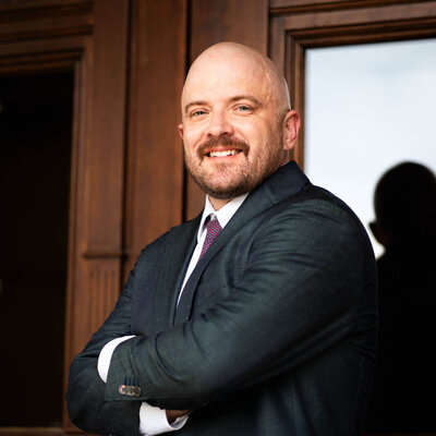 bald male attorney with facial hair in suit jacket by wooden door