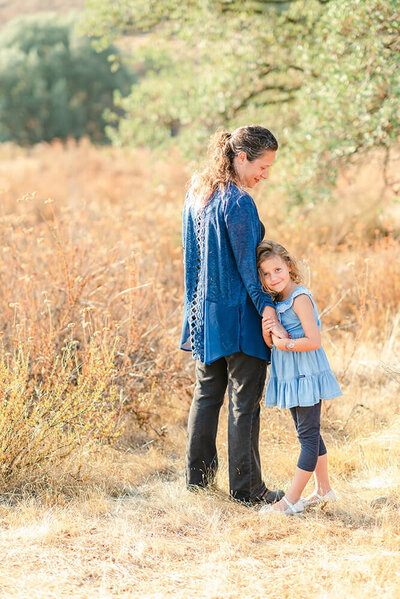 Young girl hugs her mother in a field of dry grass by Livermore family photographer Kristen Hazelton