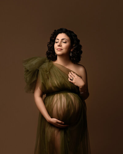 Maternity studio photo featuring a mom-to-be in a olive green tulle sheer gown with a one-shoulder poof