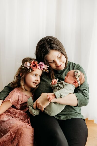 mom cuddling her two daughters, one toddler and one baby