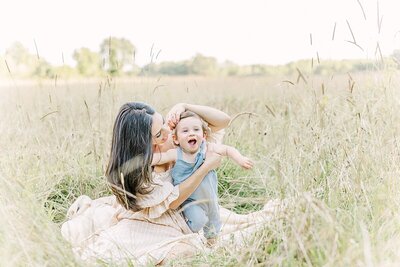 Mother sits in field with son during family photo session with Sara Sniderman Photography at Heard Farm in Wayland Massachusetts