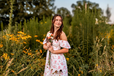 A curly brown  haired  posed next to a pond surrounded by colorful fall trees at Tower Grove park in Saint Louis, MO.