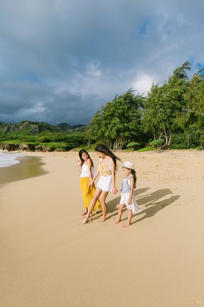 A mother walks holding hands to her two children along the beach of Kauai.
