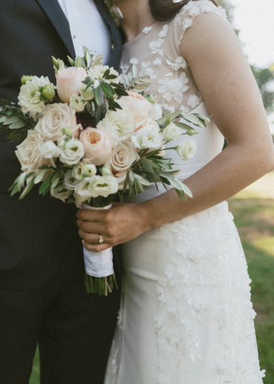A bride holding her bouquet of pale pink and white flowers embracing her groom