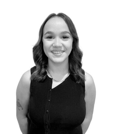 Apprentice with chin-length wavy hair and bangs, wearing a black t-shirt, representing enthusiasm and creativity in hairstyling.