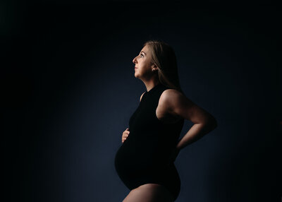 Styled Maternity Photoshoot on a dramatic dark background with mum-to-be wearing a black maternity bodysuit