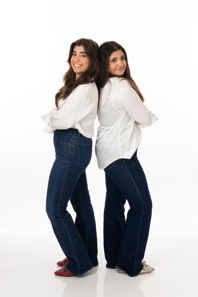 teenage sisters on simple white backdrop  with white tops and jeans with fancy shoes, simple stylish, pose family portraits 2025 High school senior
