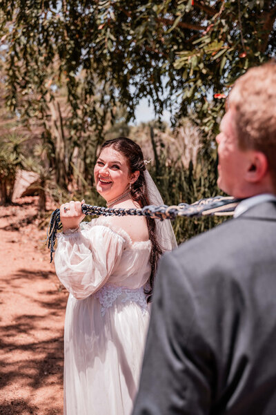A joyful bride and groom share a laugh while tying their wedding knot, capturing a moment of love and happiness.