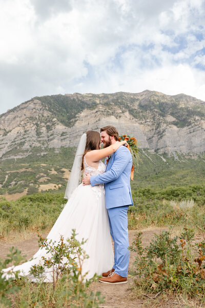 Brunette bride and brunette groom hold each other close with a gorgeous mountain view in the background.