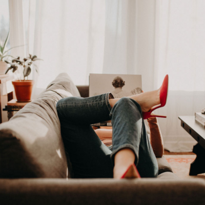 A woman in jeans and pink heels lays on a couch while holding Taylor Swift's album, Evermore.