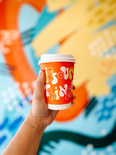 Hand holding a Quigley Coffee takeaway cup in front of colorful mural