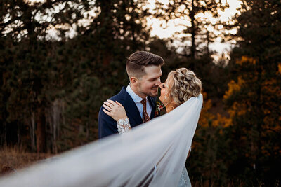 Wedding couple kissing while brides veil blows in the wind in Pine Colorado