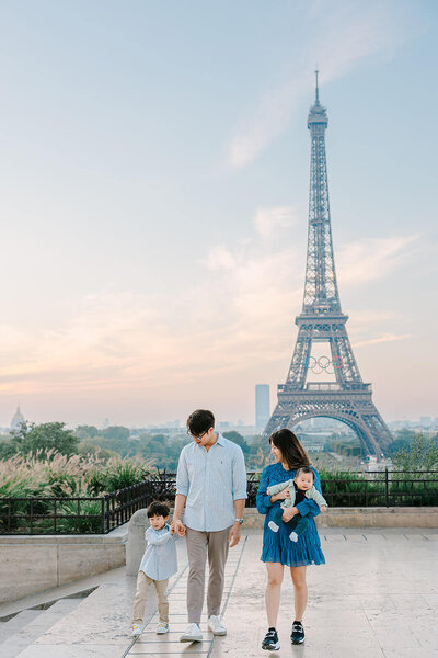 Family of four — mother, father, young boy, and baby — walking near the Eiffel Tower at Trocadéro, with the mother holding the baby during a Paris family photoshoot.