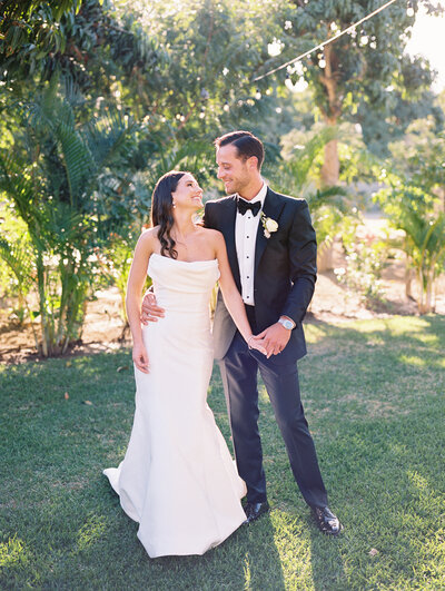Bride and groom posing together in front of trees with sunlight behind them