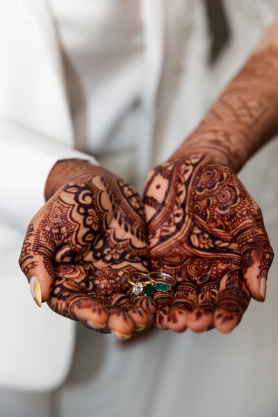 Henna tattoed hands holding wedding rings.