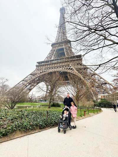 A father is standing in front of the Eiffel tower with his two daughters, captured by an Austin Texas Photographer.
